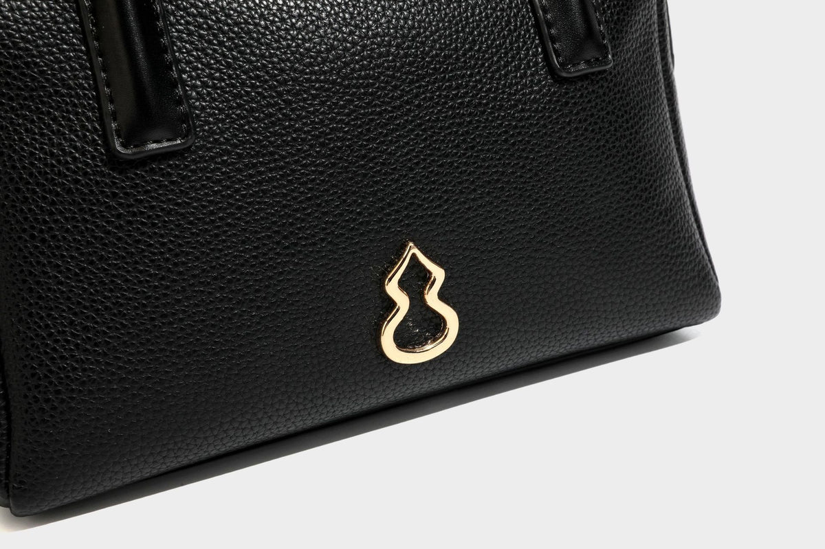 Small structured pillow satchel bag with pebbled leather-look finish, dual rolled top handles, gold-tone gourd emblem, and