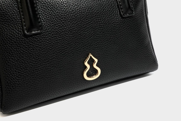 Small structured pillow satchel bag with pebbled leather-look finish, dual rolled top handles, gold-tone gourd emblem, and