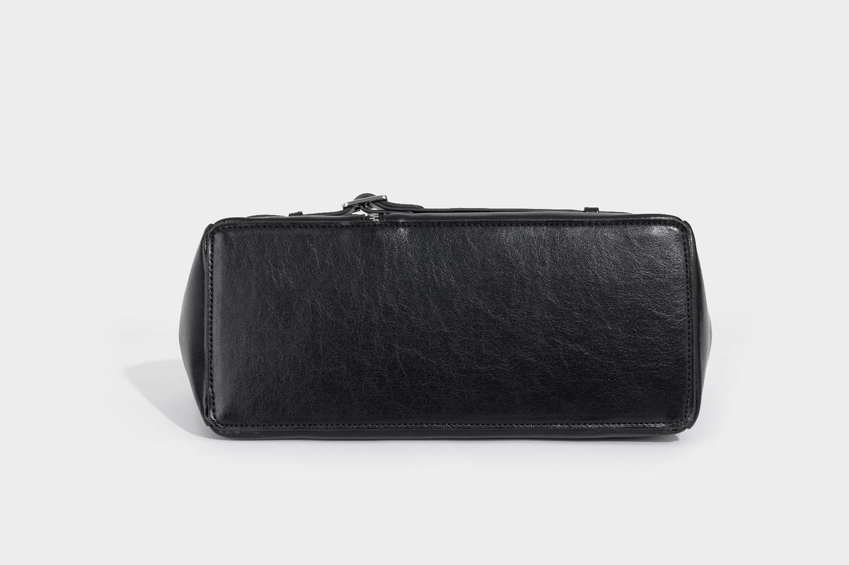 Structured black leather-look satchel bag with silver padlock hardware, front zip pockets, key charms, and top handles