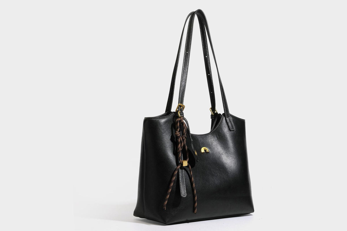 Structured smooth leather-look tote bag with long shoulder strap, gold-tone hardware, and hanging tassel-coin charm, detail
