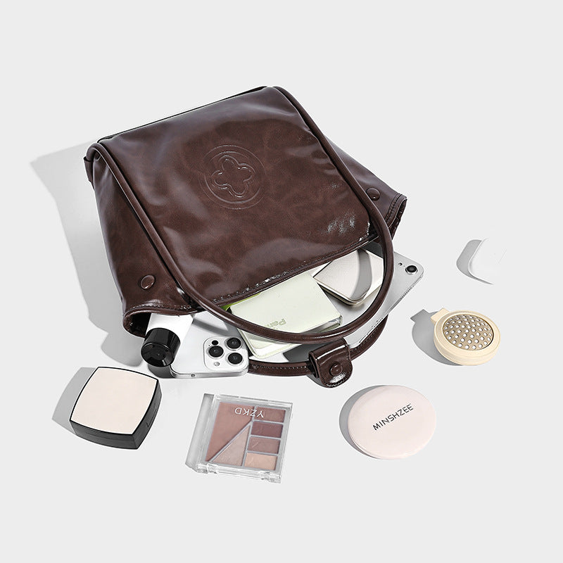 Glossy leather-look structured tote bag with rounded top handles, detachable shoulder strap, embossed front emblem, and side