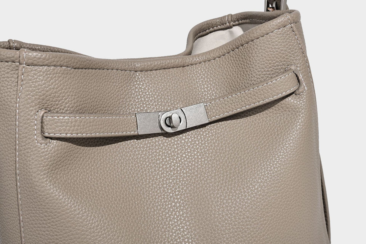 Soft-structured pebbled bucket shoulder bag with front turn-lock strap detail, adjustable strap, and hanging floral tassel