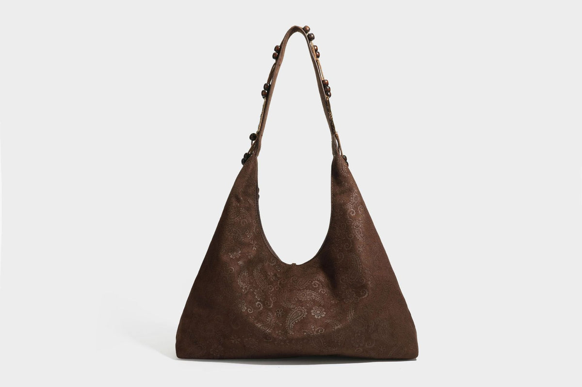 Slouchy boho hobo shoulder bag in embossed brown suede-look finish with beaded strap, cord tassels, and brass-tone leaf