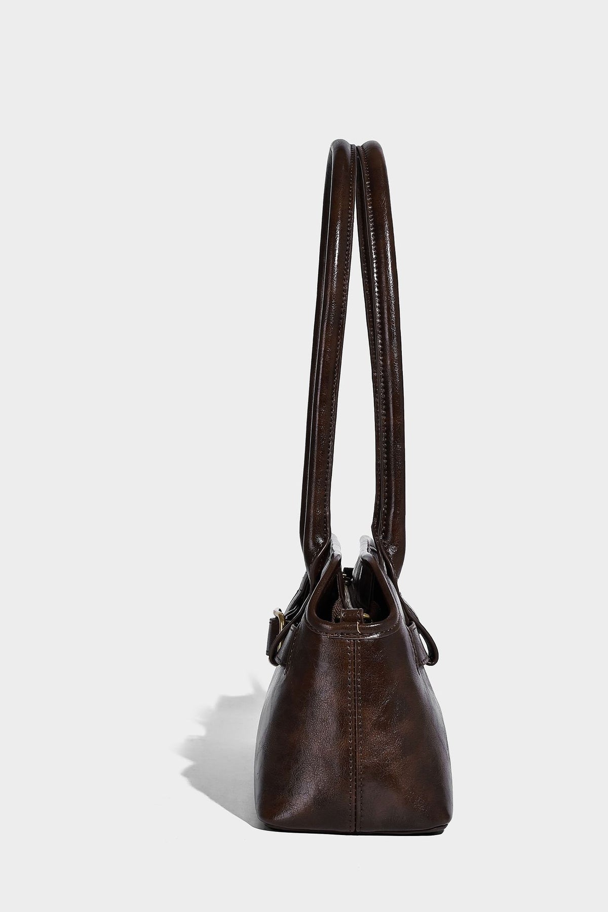 Strukturierte dunkelbraune Henkeltasche mit Öl-Wachs-Finish, vorderer Gürtelschnalle, goldfarbenen Beschlägen und zwei Tragegriffen, Detailansicht