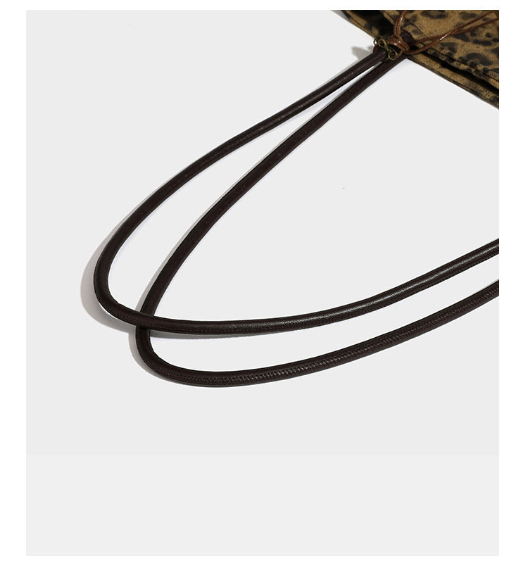 Large leopard print shoulder tote bag in tan and brown with slim dark straps and dangling beaded charm hardware, detail view