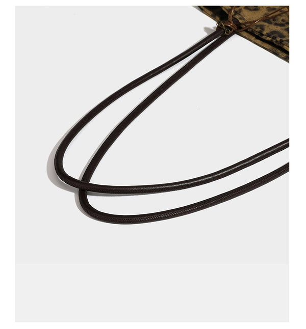 Large leopard print shoulder tote bag in tan and brown with slim dark straps and dangling beaded charm hardware, detail view