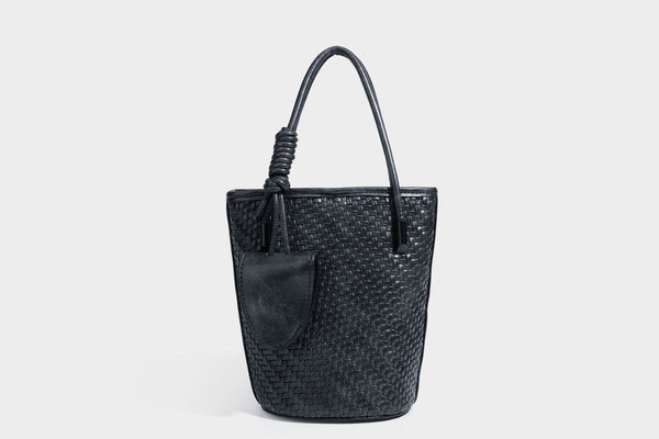 Structured woven-texture leather-look bucket bag in brown with knotted top handles, small front flap pouch, and adjustable
