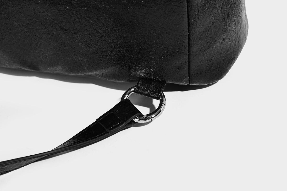 Glossy black convertible bucket backpack with silver grommet-studded straps, drawstring cinch closure, and front zip pocket