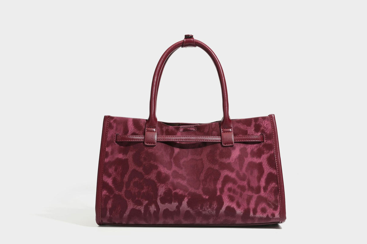 Structured leopard-print tote bag with glossy satin-like finish, dual rounded top handles, silver buckle-and-ring front