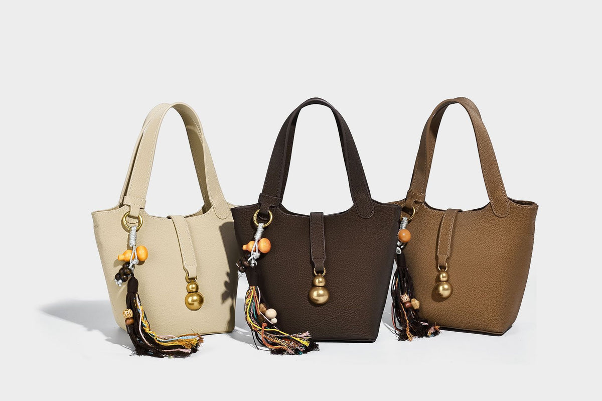 Kleine matte Beuteltasche mit genarbter Oberfläche, antikgoldfarbenen Ringbeschlägen, Perlen- und Quastenanhänger, kurzen Tragegriffen oben und