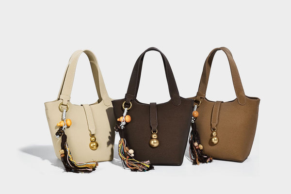 Kleine matte Beuteltasche mit genarbter Oberfläche, antikgoldfarbenen Ringbeschlägen, Perlen- und Quastenanhänger, kurzen Tragegriffen oben und