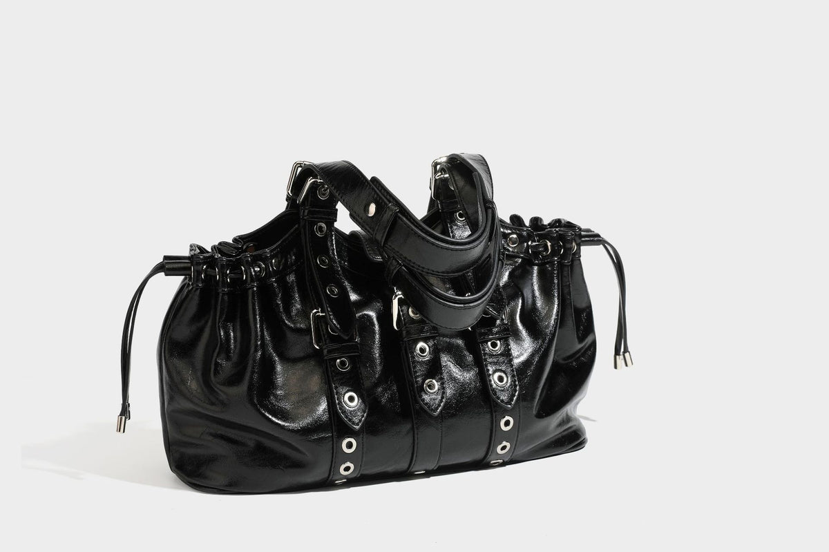 Large black glossy leather-look tote bag with silver buckle straps, eyelet grommet panels, drawstring side gathers, and