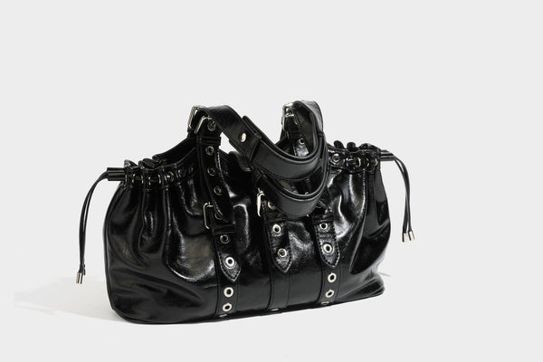 Large black glossy leather-look tote bag with silver buckle straps, eyelet grommet panels, drawstring side gathers, and
