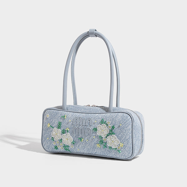 Small structured light blue denim-texture bowling bag with white floral bead embroidery, dual rounded top handles, and, front