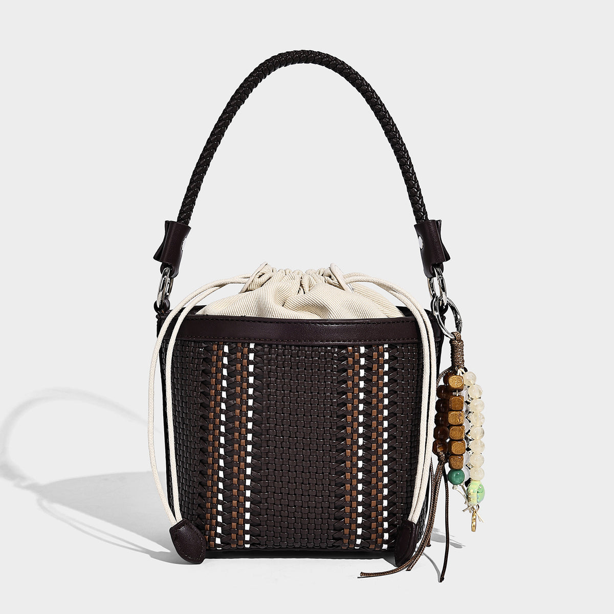 Small woven bucket bag with drawstring top, braided handle, detachable crossbody strap, and silver-tone ring hardware, detail
