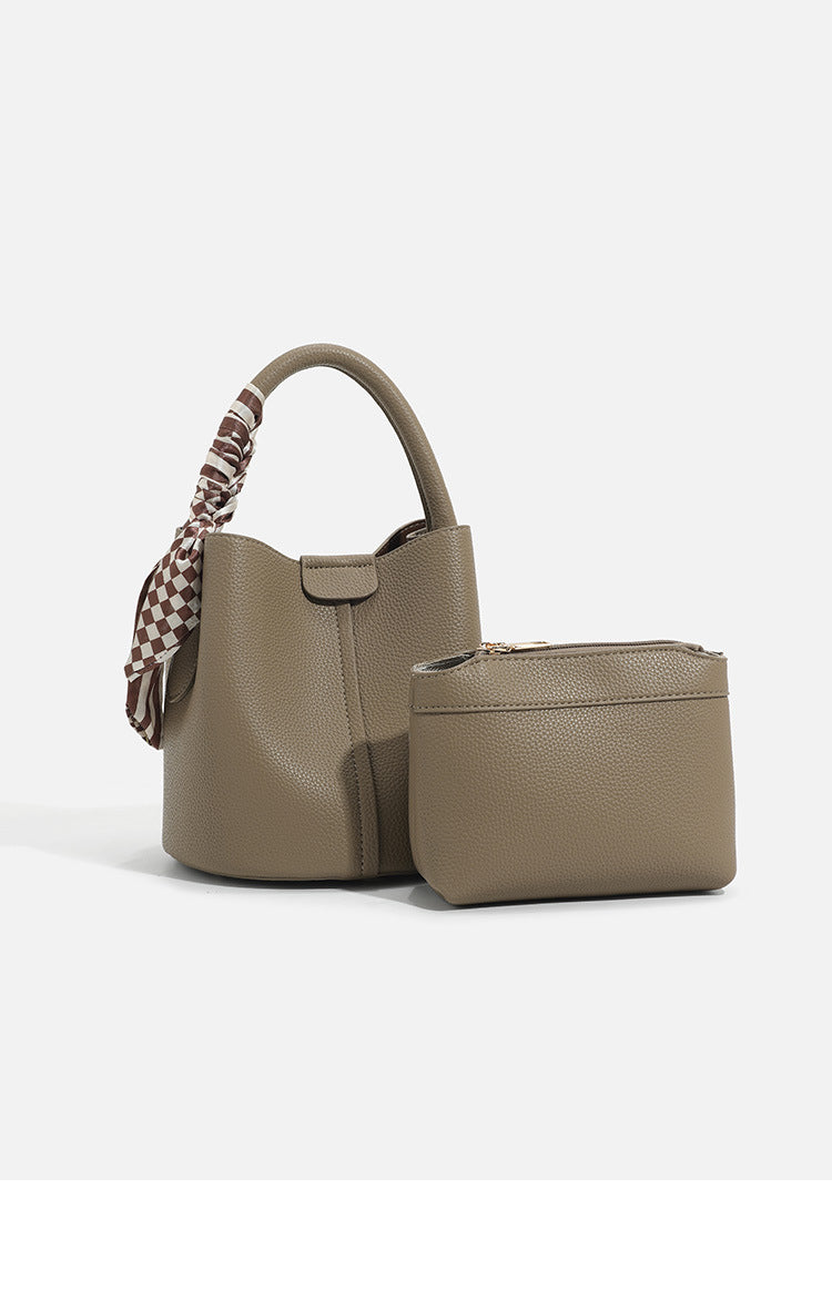 Pebbled leather-look bucket bag with checkered scarf-wrapped top handle, flap tab closure, gold-tone hardware, and matching