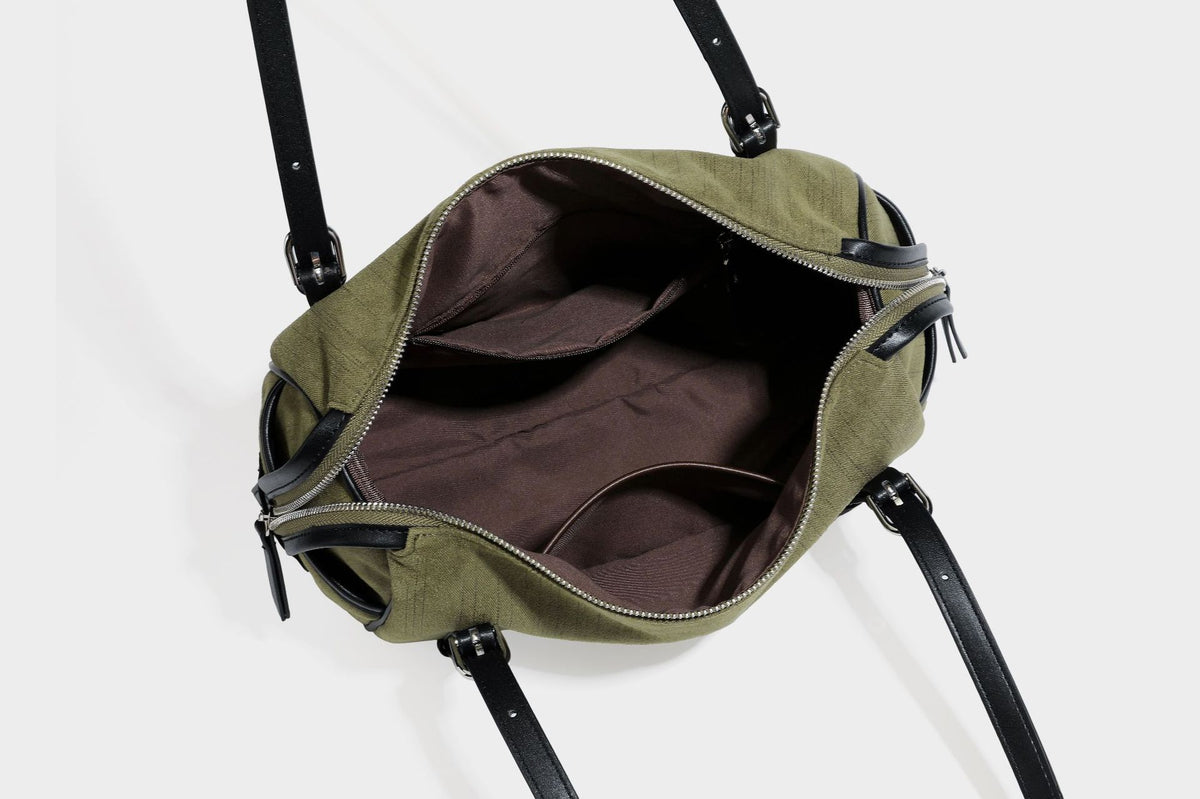 Olivgrüne Canvas-Schultertasche in Zylinderform mit schwarzen Trägern in Lederoptik, Reißverschluss oben und silberfarbenen Metallbeschlägen, Detailansicht