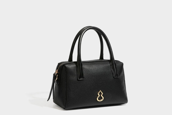 Small structured pillow satchel bag with pebbled leather-look finish, dual rolled top handles, gold-tone gourd emblem, and