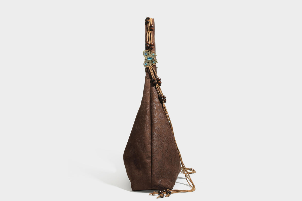 Slouchy boho hobo shoulder bag in embossed brown suede-look finish with beaded strap, cord tassels, and brass-tone leaf