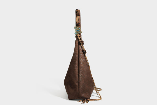 Slouchy boho hobo shoulder bag in embossed brown suede-look finish with beaded strap, cord tassels, and brass-tone leaf