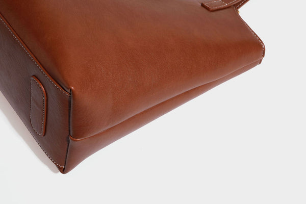 Structured smooth leather-look tote bag with long shoulder strap, gold-tone hardware, and hanging tassel-coin charm, detail