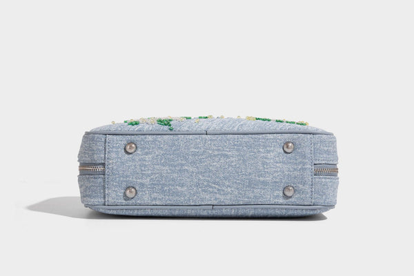 Small structured light blue denim-texture bowling bag with white floral bead embroidery, dual rounded top handles, and