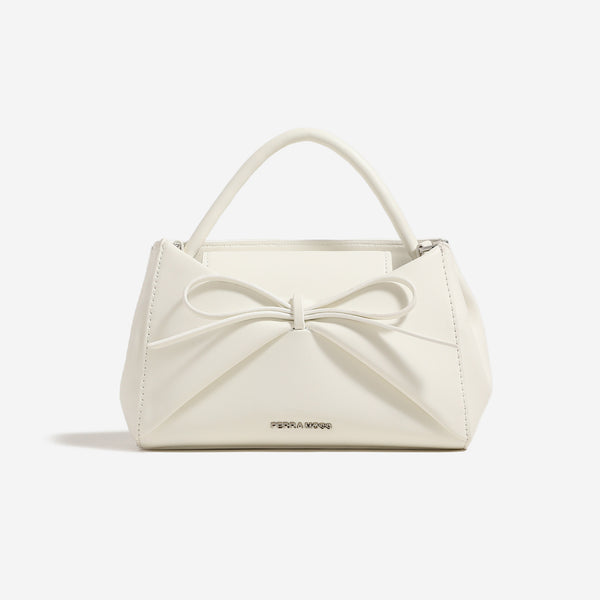 Small structured trapezoid handbag with a three-dimensional front bow, short top handle, and detachable shoulder strap