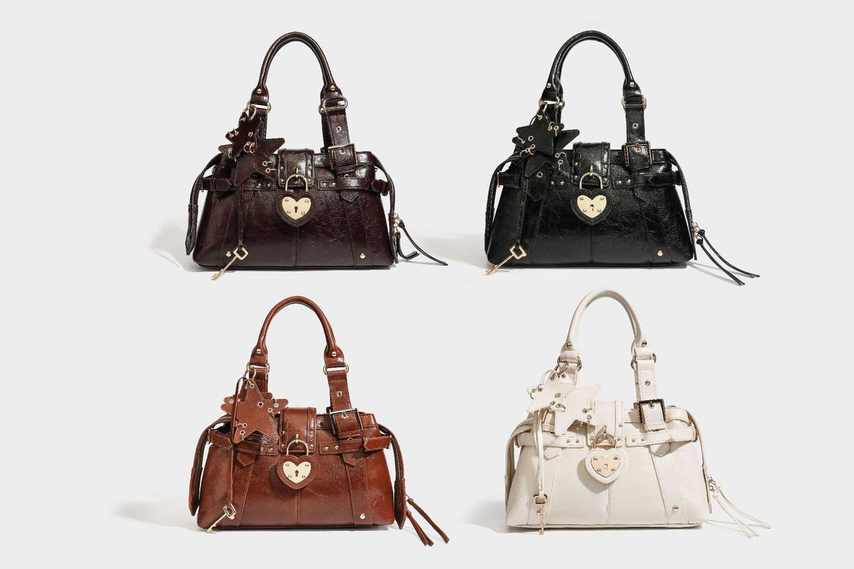 Structured leather-look satchel bag with heart padlock charm, star charm, gold-tone buckle hardware, dual top handles, and