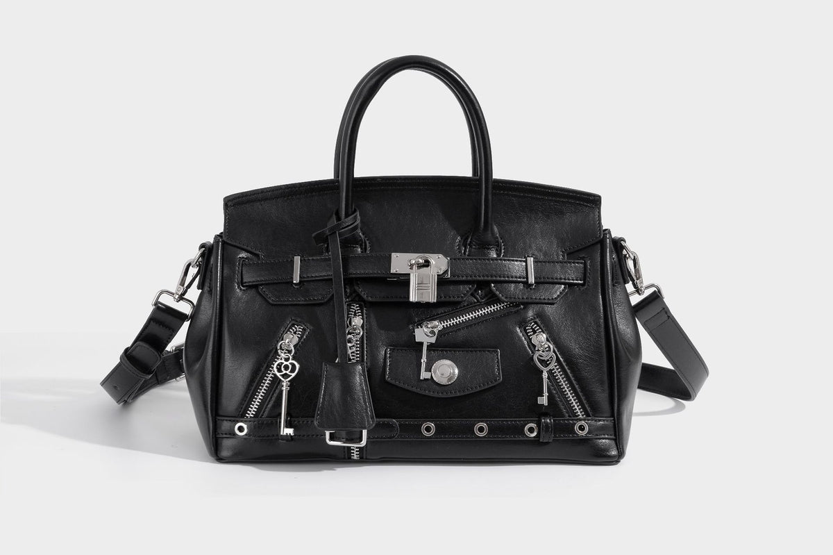 Structured black leather-look satchel bag with silver padlock hardware, front zip pockets, key charms, and top handles