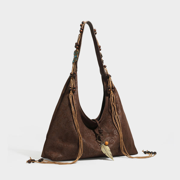 Slouchy boho hobo shoulder bag in embossed brown suede-look finish with beaded strap, cord tassels, and brass-tone leaf