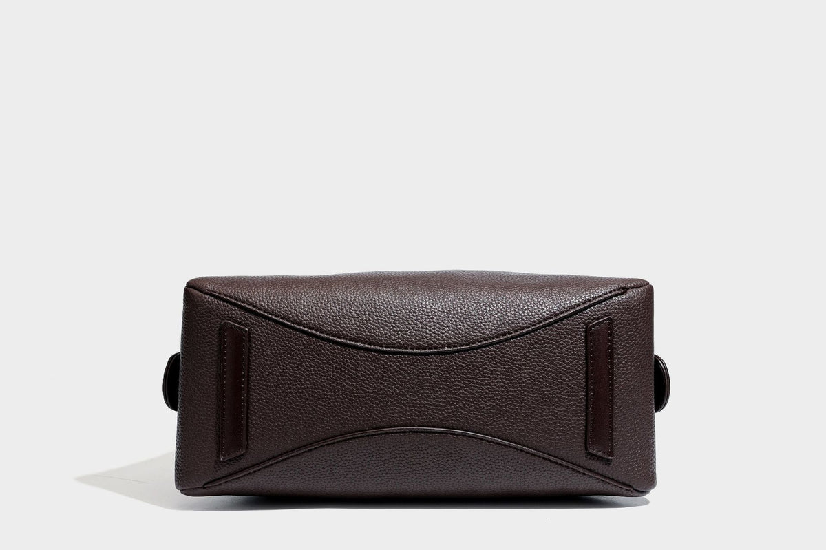 Structured trapezoid shoulder bag in dark brown pebbled leather-look finish with slim double straps, top zip closure, side