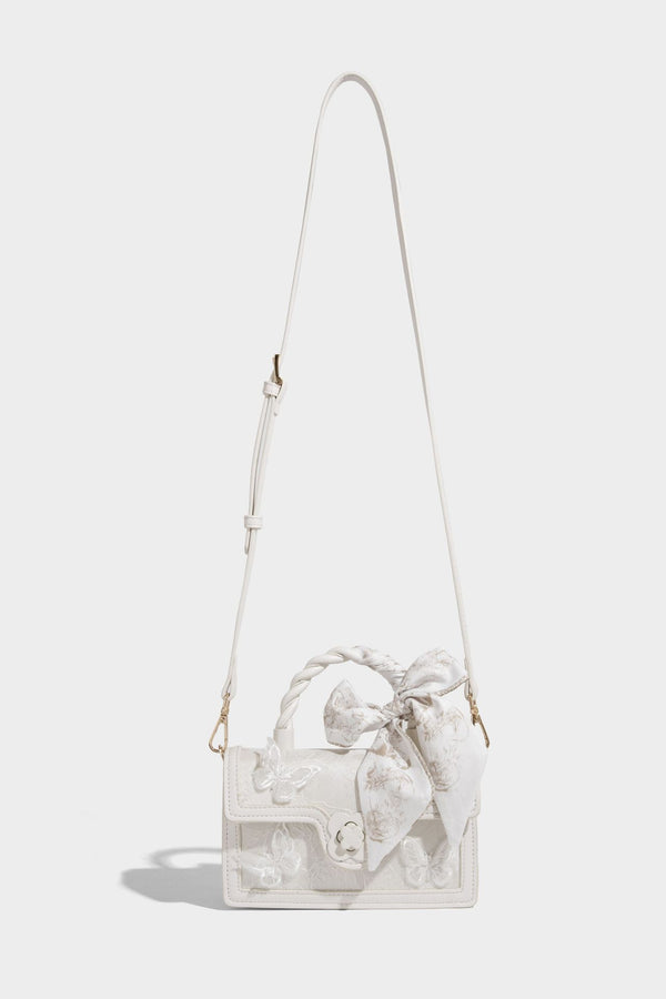 Small structured white flap bag with butterfly embroidery, flower-shaped turn-lock clasp, braided top handle with scarf bow