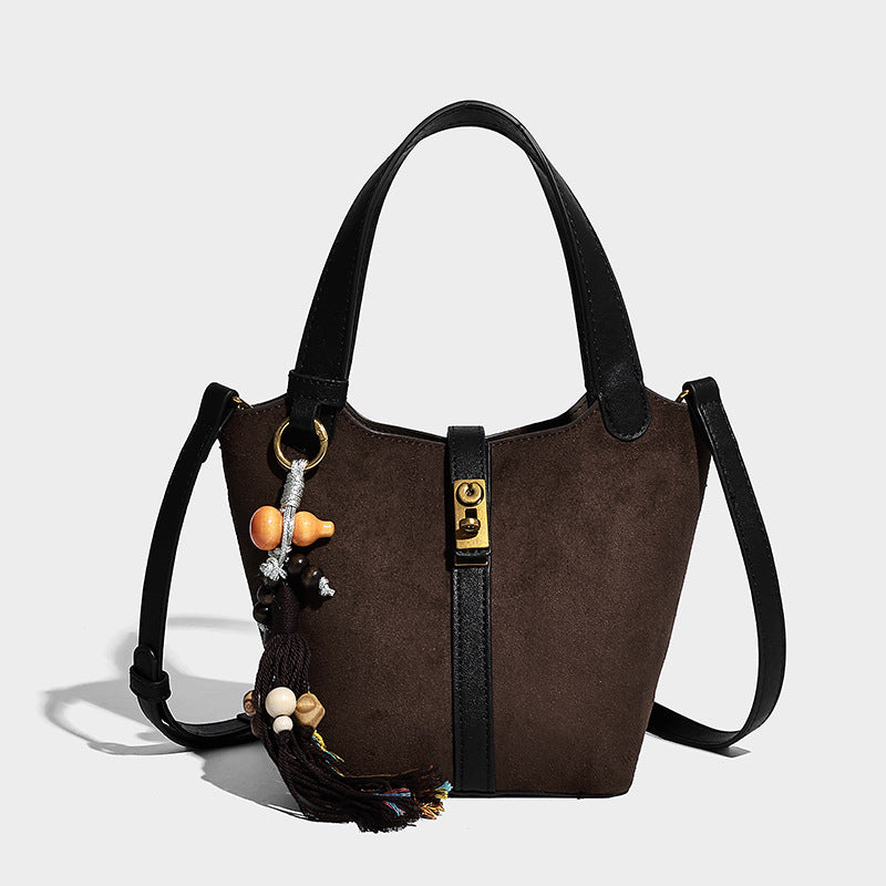 Small structured trapezoid tote bag in matte suede-look finish with black contrast trim, gold-tone front clasp, tassel charm