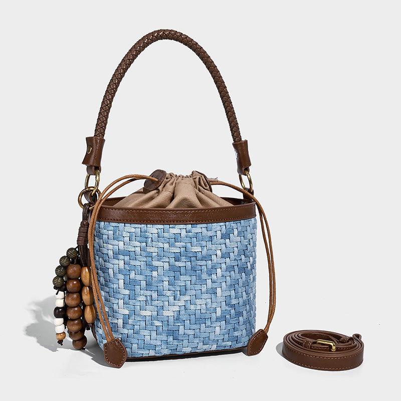 Small light blue woven bucket bag with brown leather-look trim, braided top handle, brass-tone ring hardware, drawstring