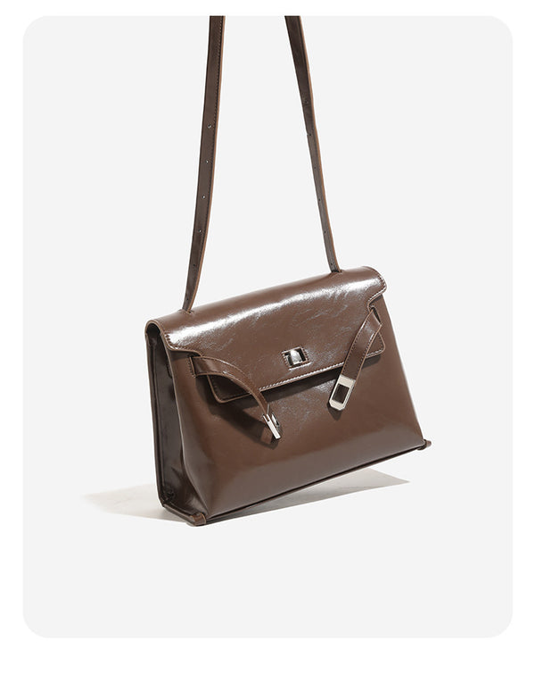 Structured trapezoidal flap satchel bag with silver-tone turn-lock clasp, decorative front strap tabs, gusseted sides, and