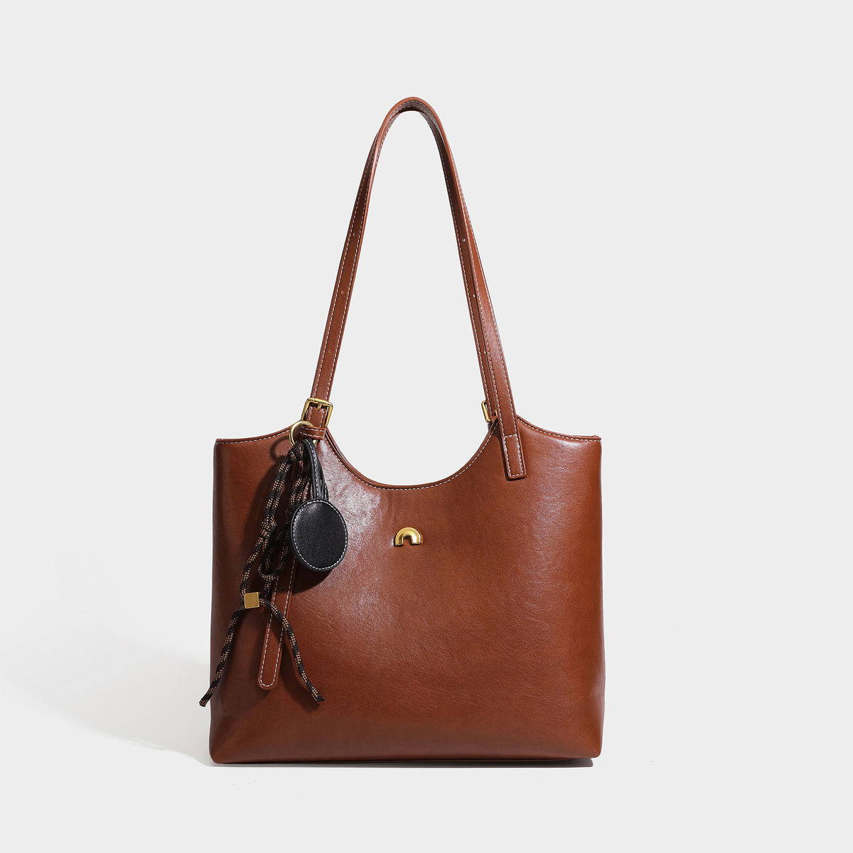 Structured smooth leather-look tote bag with long shoulder strap, gold-tone hardware, and hanging tassel-coin charm, detail