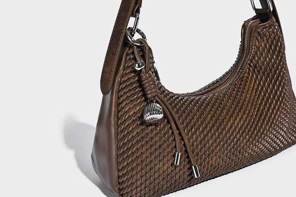 Woven crescent hobo shoulder bag with smooth side panels, zip-top closure, silver-tone charm hardware, and adjustable, detail