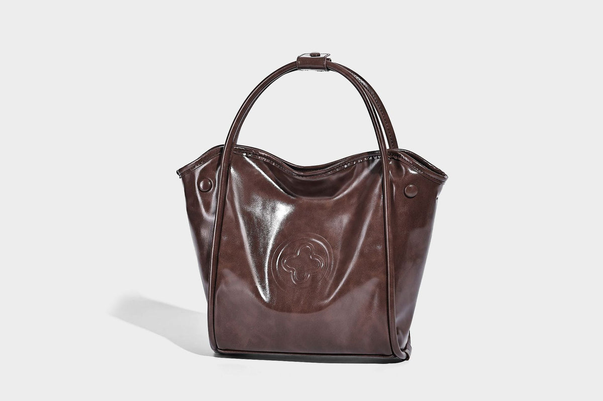 Glossy leather-look structured tote bag with rounded top handles, detachable shoulder strap, embossed front emblem, and side