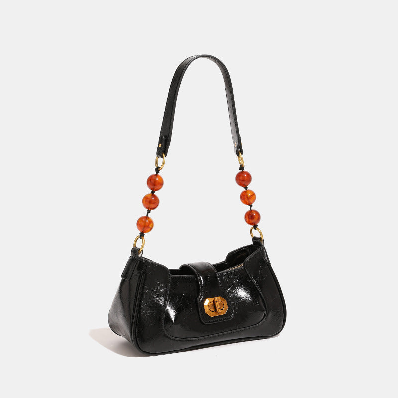 Structured glossy crinkled-finish shoulder bag with amber resin bead strap accent and gold-tone turn-lock closure, detail