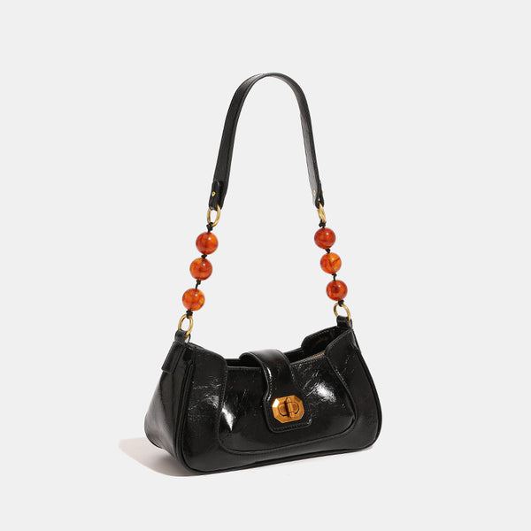 Structured glossy crinkled-finish shoulder bag with amber resin bead strap accent and gold-tone turn-lock closure, detail