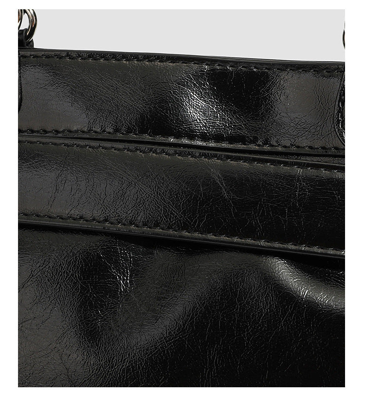 Black glossy structured tote bag with rivet and buckle detail, dual top handles, and detachable shoulder strap, detail view