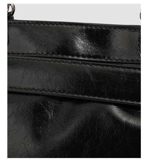 Black glossy structured tote bag with rivet and buckle detail, dual top handles, and detachable shoulder strap, detail view