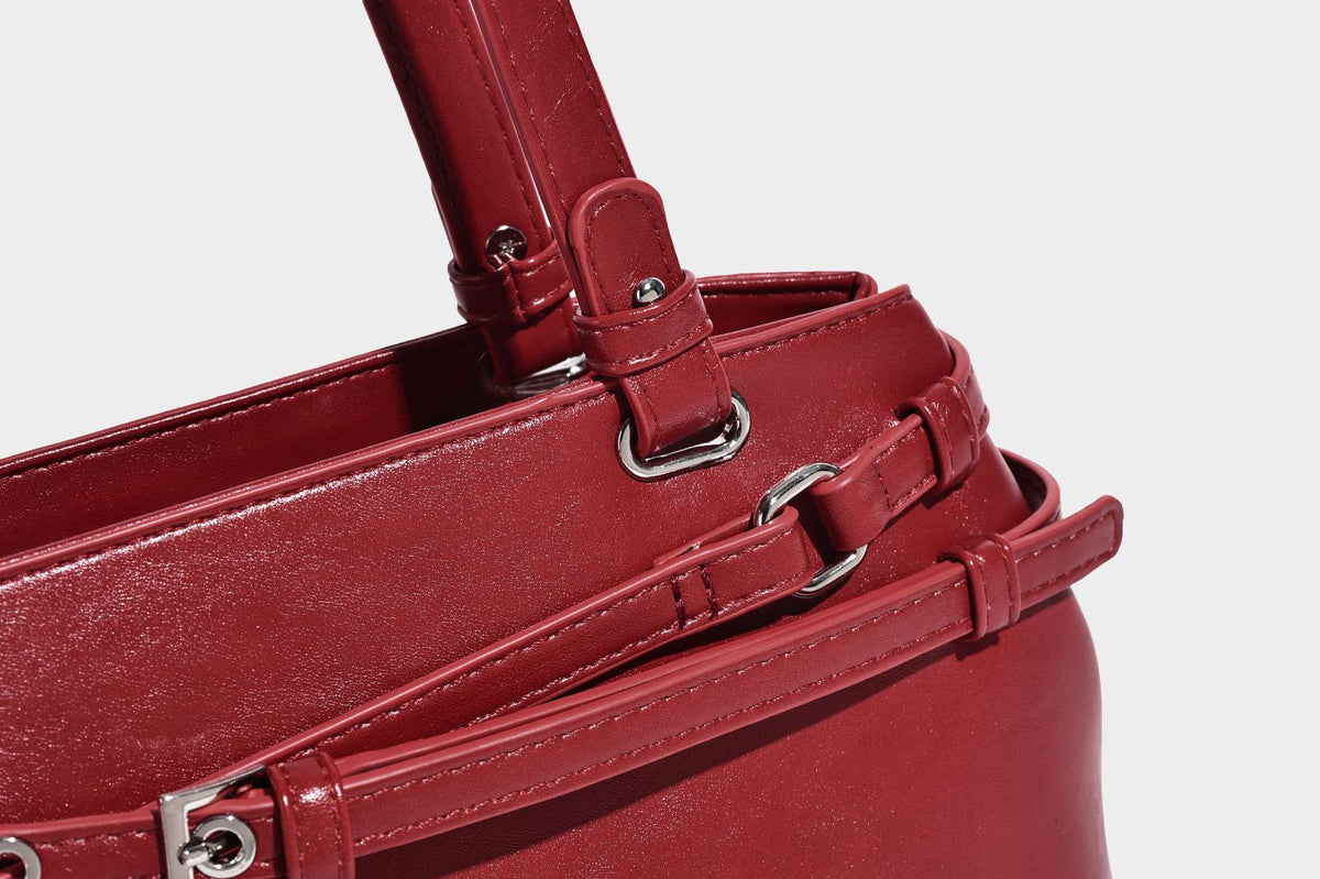 Structured glossy leather-look shoulder bag with wraparound belt straps, silver-tone hardware, and dangling star charm