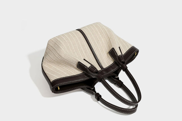 Cremefarbene geflochtene Tote-Bag mit dunkelbraunen Besätzen in Lederoptik, kontrastierenden weißen Nähten, zwei oberen Henkeln und abnehmbarem Schulter