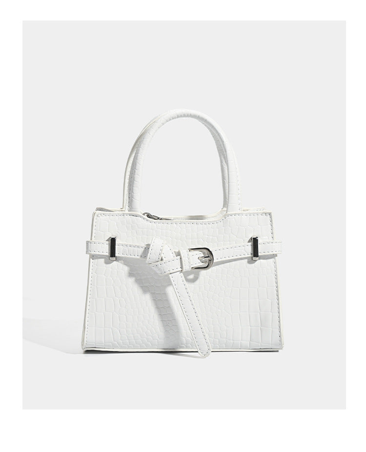 Small structured trapezoid mini top-handle bag with front belt-knot buckle detail and glossy leather-look finish, detail view