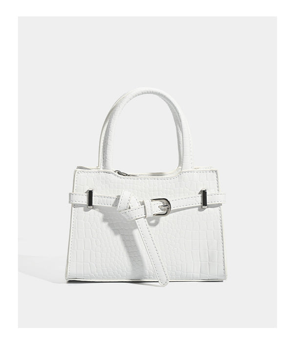 Small structured trapezoid mini top-handle bag with front belt-knot buckle detail and glossy leather-look finish, detail view