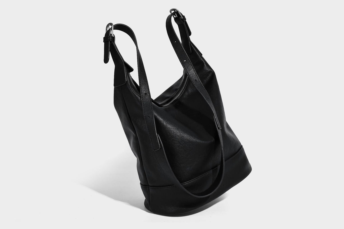 Slouchy bucket hobo shoulder bag in dark brown with glossy leather-look finish, top zip closure, and long adjustable, detail
