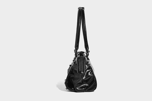 Längliche Schultertasche in Zylinderform mit glänzender Lederoptik, silberfarbenen Nietenbeschlägen, seitlichen Quasten und mehreren außenliegenden Reißverschlüssen