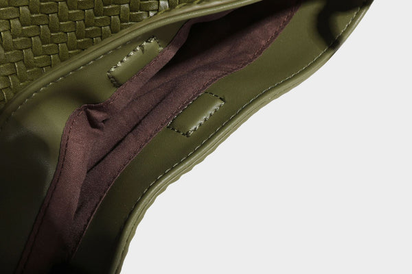 Olive green woven leather-look bucket bag with braided crossbody strap, knotted adjustment, and gold-tone tassel charm with