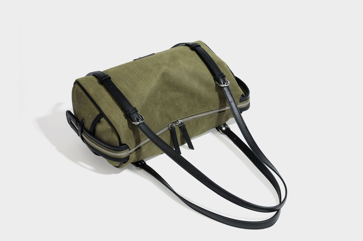 Olivgrüne Canvas-Schultertasche in Zylinderform mit schwarzen Trägern in Lederoptik, Reißverschluss oben und silberfarbenen Metallbeschlägen, Detailansicht